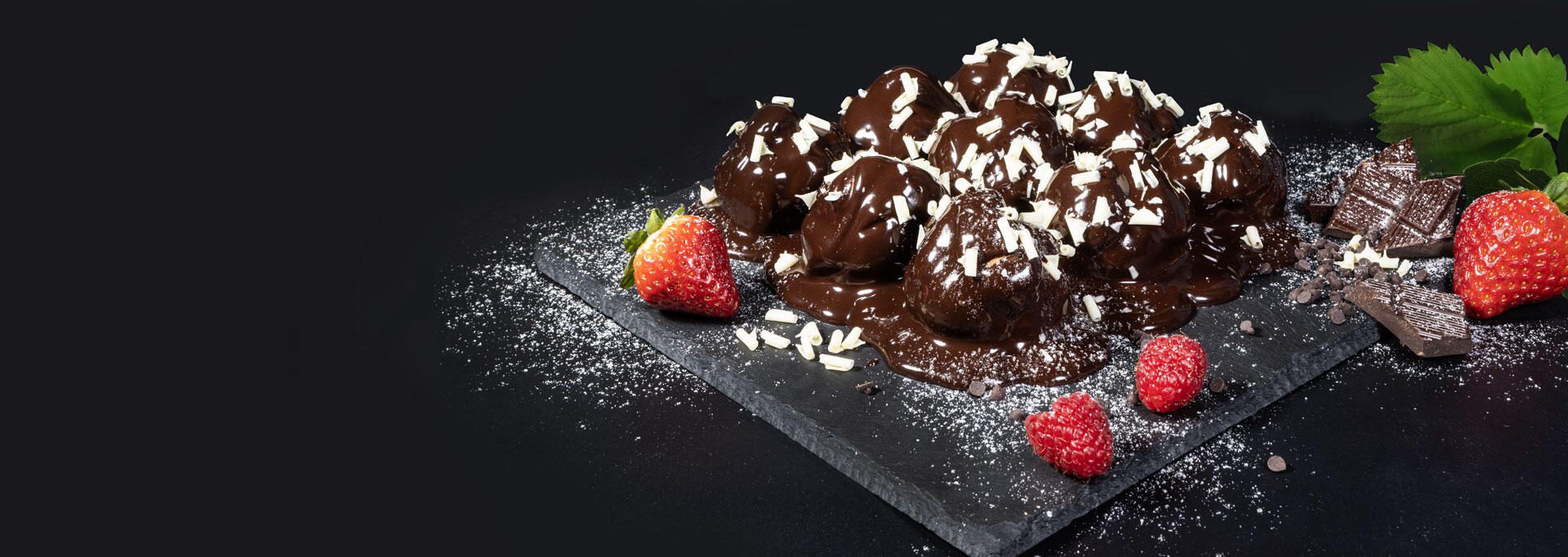 piatto con profitterol con decorazioni di pezzi di cioccolato, lamponi, fragole e menta.